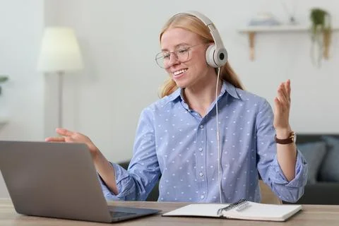 Interpreter in headphones having video chat via laptop at table indoors Stock Photos