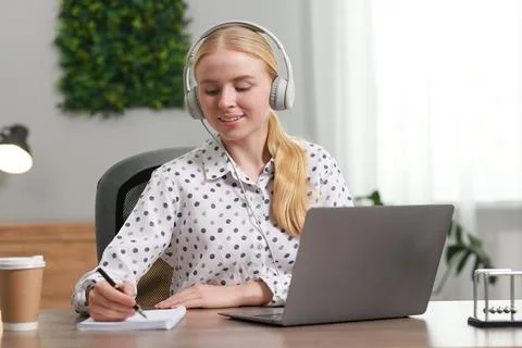 Interpreter in headphones taking notes while working with laptop at table i.. Stock Photos