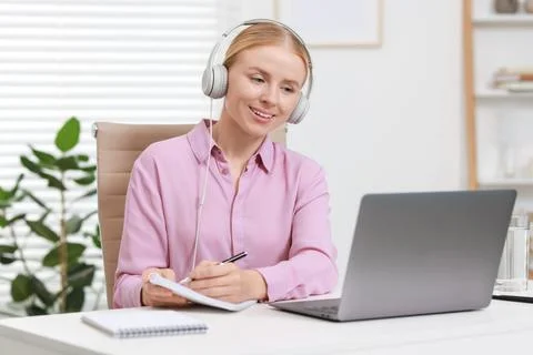 Interpreter in headphones taking notes while having video chat via laptop a.. Stock Photos