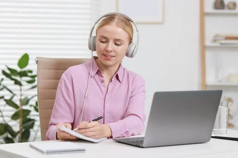 Interpreter in headphones taking notes while having video chat via laptop a.. Stock Photos