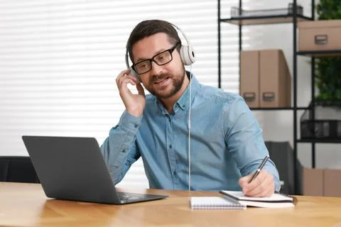 Interpreter in headphones taking notes while having video chat via laptop a.. Stock Photos