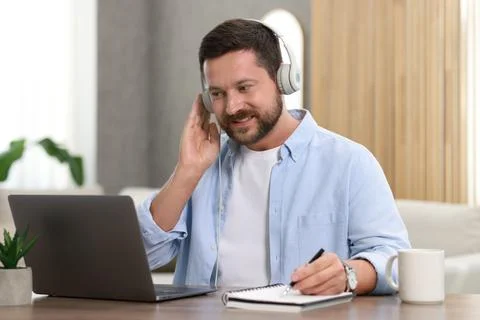 Interpreter in headphones taking notes while having video chat via laptop a.. Stock Photos