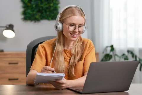 Interpreter in headphones taking notes while having video chat via laptop a.. Stock Photos
