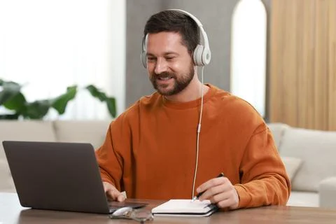 Interpreter in headphones taking notes while having video chat via laptop a.. Stock Photos