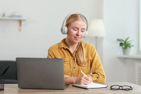 Interpreter in headphones taking notes while working with laptop at table i.. Stock Photos