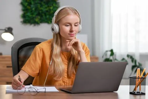 Interpreter in headphones taking notes while working with laptop at table i.. Stock Photos