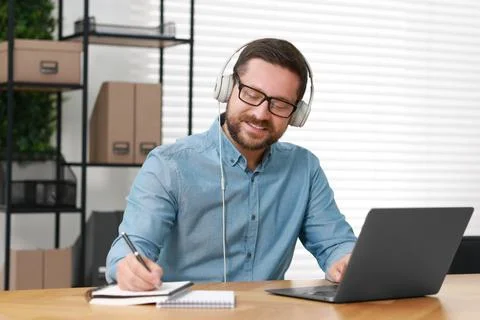 Interpreter in headphones taking notes while having video chat via laptop a.. Stock Photos
