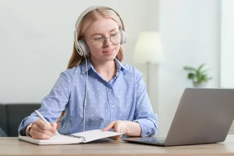 Interpreter in headphones taking notes while working with laptop at table i.. Stock Photos