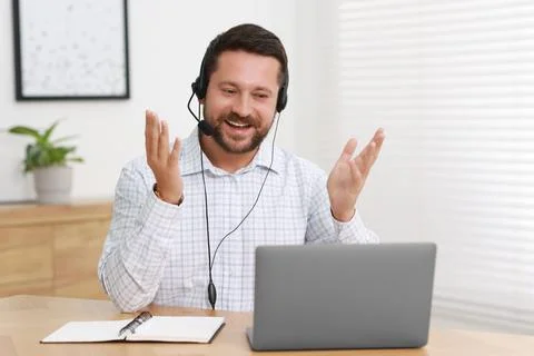 Interpreter in headset having video chat via laptop at wooden table indoors Stock Photos