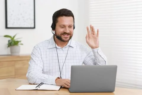 Interpreter in headset having video chat via laptop at wooden table indoors Stock Photos