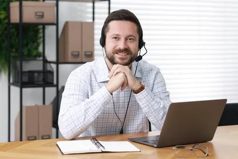 Interpreter in headset having video chat via laptop at wooden table indoors Stock Photos