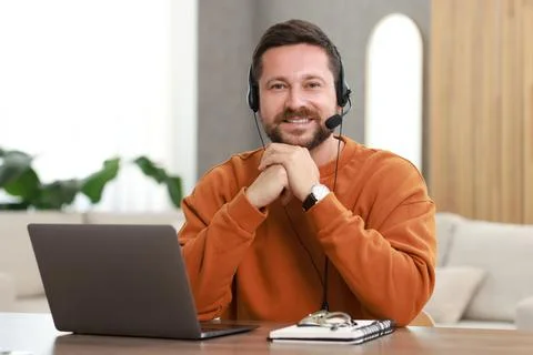 Interpreter in headset having video chat via laptop at wooden table indoors Stock Photos