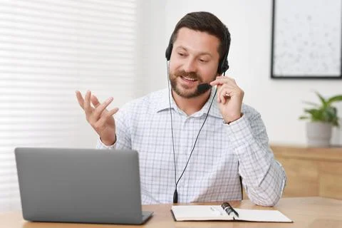 Interpreter in headset having video chat via laptop at wooden table indoors Stock Photos