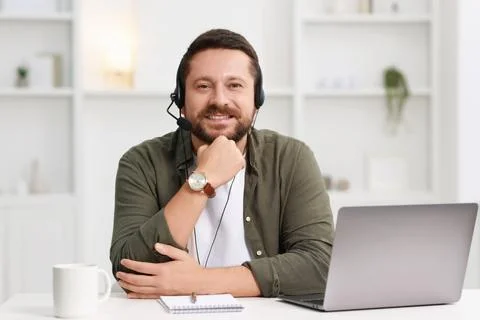 Interpreter in headset having video chat via laptop at white table indoors Stock Photos