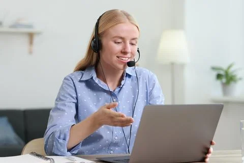 Interpreter in headset having video chat via laptop at table indoors Stock Photos