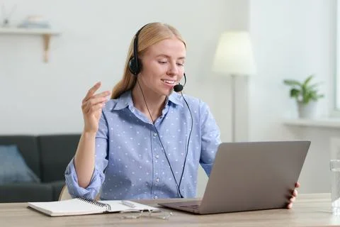 Interpreter in headset having video chat via laptop at table indoors Stock Photos