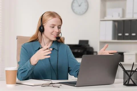 Interpreter in headset having video chat via laptop at table indoors Stock Photos