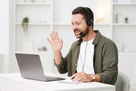 Interpreter in headset having video chat via laptop at white table indoors Stock Photos