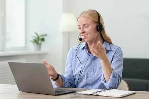 Interpreter in headset having video chat via laptop at table indoors Stock Photos