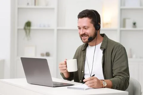 Interpreter in headset having video chat via laptop at white table indoors Stock Photos