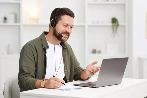 Interpreter in headset having video chat via laptop at white table indoors Stock Photos