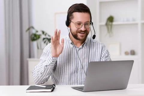 Interpreter in headset having video chat via laptop at white table indoors Stock Photos