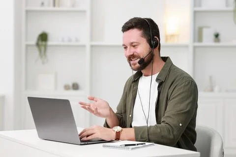 Interpreter in headset having video chat via laptop at white table indoors Stock Photos