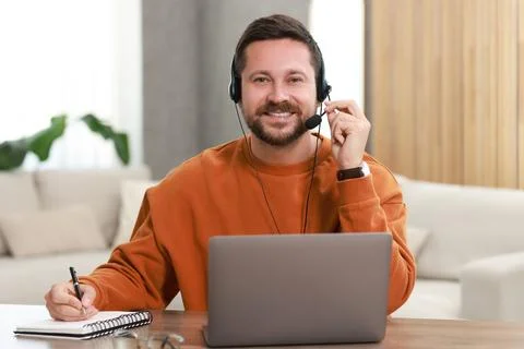 Interpreter in headset having video chat via laptop at wooden table indoors Stock Photos