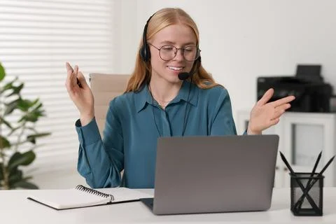 Interpreter in headset having video chat via laptop at table indoors Stock Photos