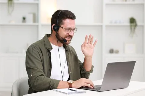 Interpreter in headset having video chat via laptop at white table indoors Stock Photos