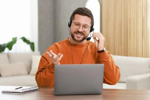 Interpreter in headset having video chat via laptop at wooden table indoors Stock Photos