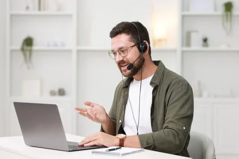 Interpreter in headset having video chat via laptop at white table indoors Stock Photos