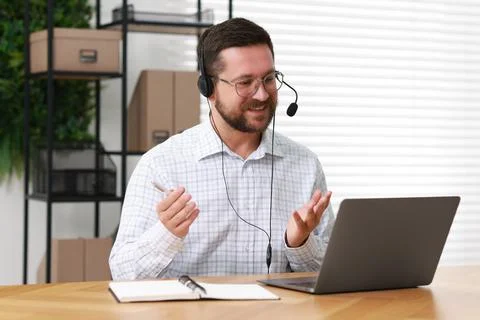 Interpreter in headset having video chat via laptop at wooden table indoors Stock Photos