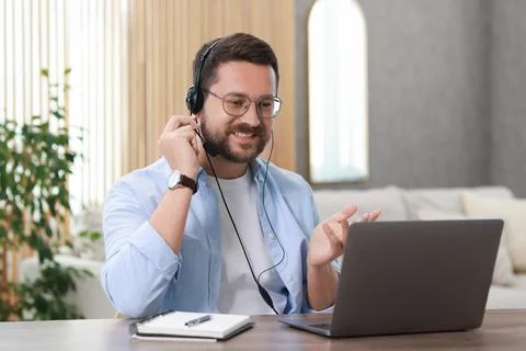 Interpreter in headset having video chat via laptop at wooden table indoors Stock Photos