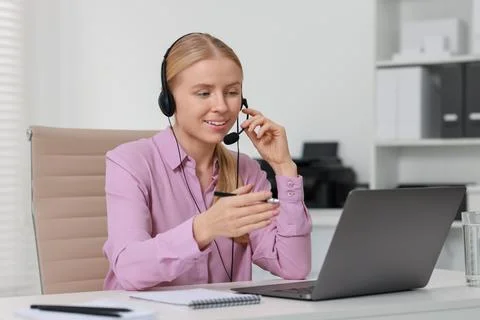 Interpreter in headset having video chat via laptop at table indoors Stock Photos