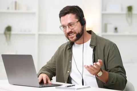 Interpreter in headset having video chat via laptop at white table indoors Stock Photos
