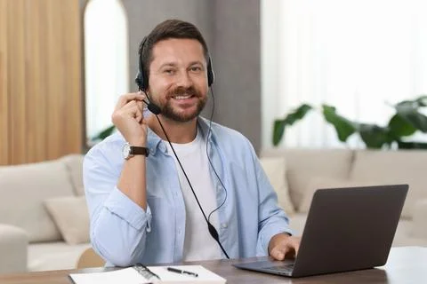 Interpreter in headset having video chat via laptop at wooden table indoors Stock Photos