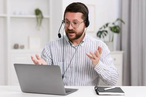 Interpreter in headset having video chat via laptop at white table indoors Stock Photos