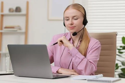 Interpreter in headset having video chat via laptop at table indoors Stock Photos