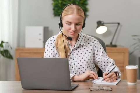 Interpreter in headset taking notes while working with laptop at table indoor Stock Photos
