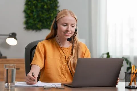 Interpreter in headset taking notes while working with laptop at table indoor Stock Photos
