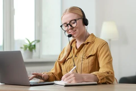 Interpreter in headset taking notes while working with laptop at table indoor Stock Photos