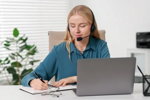 Interpreter in headset taking notes while working with laptop at table indoor Stock Photos
