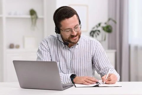 Interpreter in headset taking notes while having video chat via laptop at w.. Stock Photos