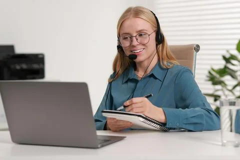 Interpreter in headset taking notes while working with laptop at table indoor Stock Photos