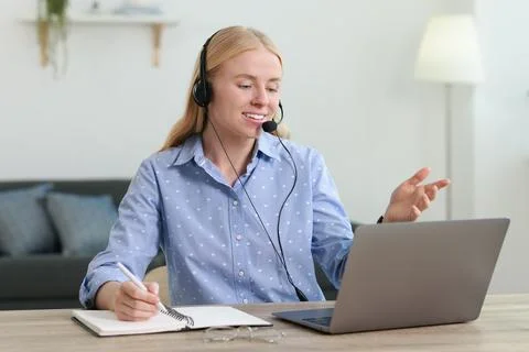 Interpreter in headset taking notes while working with laptop at table indoor Stock Photos