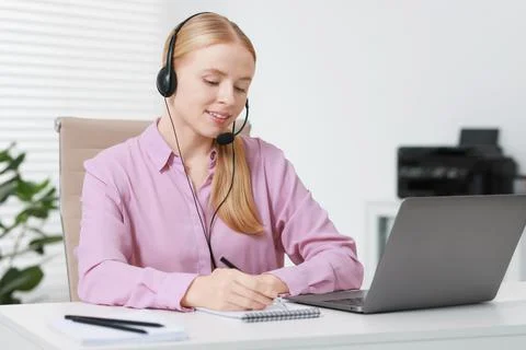 Interpreter in headset taking notes while having video chat via laptop at t.. Stock Photos