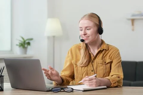 Interpreter in headset taking notes while having video chat via laptop at t.. Stock Photos