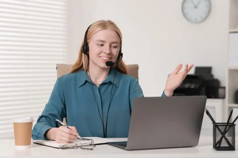 Interpreter in headset taking notes while having video chat via laptop at t.. Stock Photos