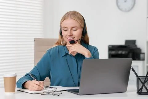 Interpreter in headset taking notes while working with laptop at table indoor Stock Photos
